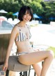 A woman in a bikini sitting on a stool by a pool.